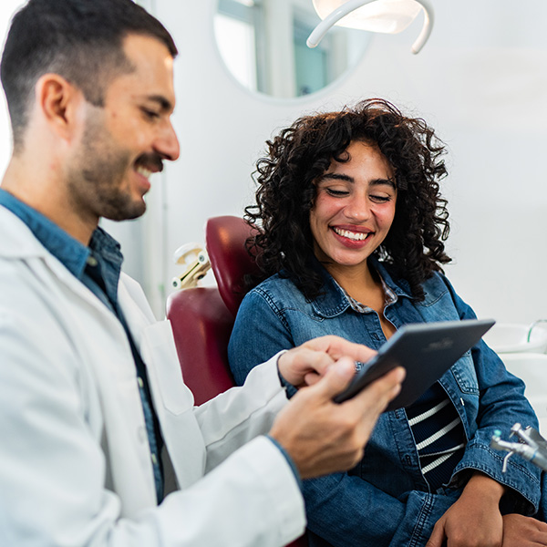 Man using digital tablet and talking to young patient woman at dentist's office